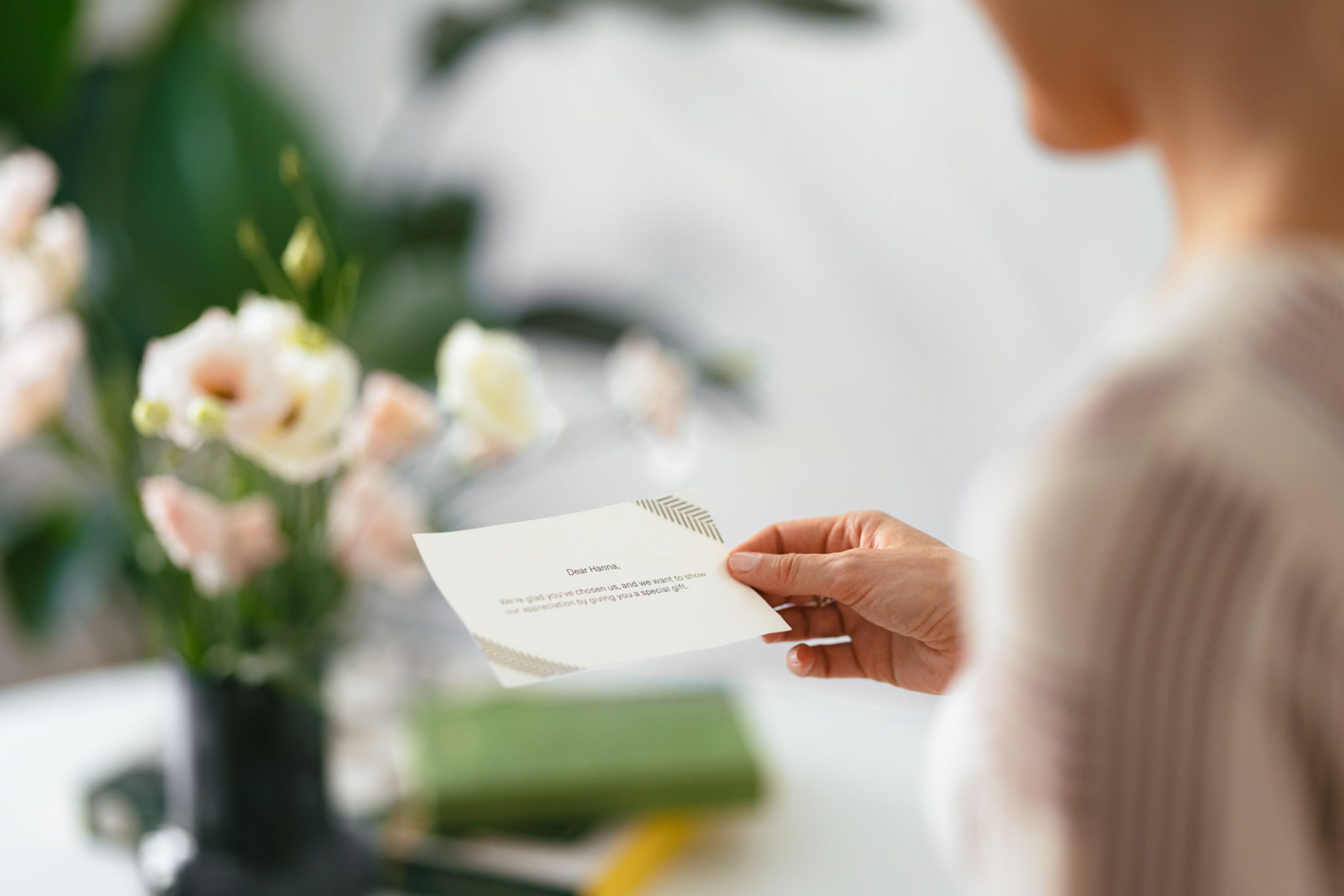 Person holding greeting card near vase of flowers